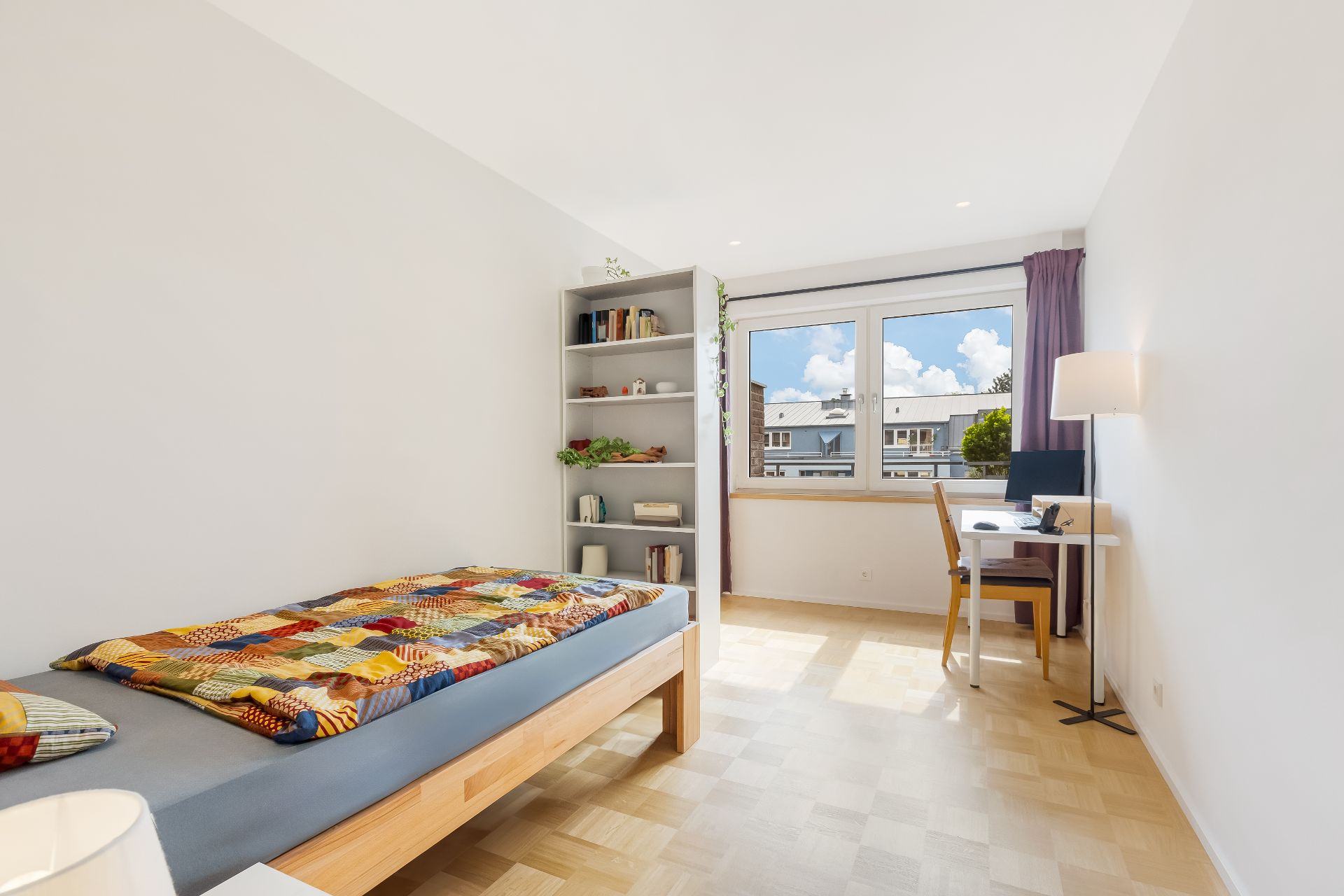 Helles Schlafzimmer mit Einzelbett, Schreibtisch, Regal und großem Fenster.