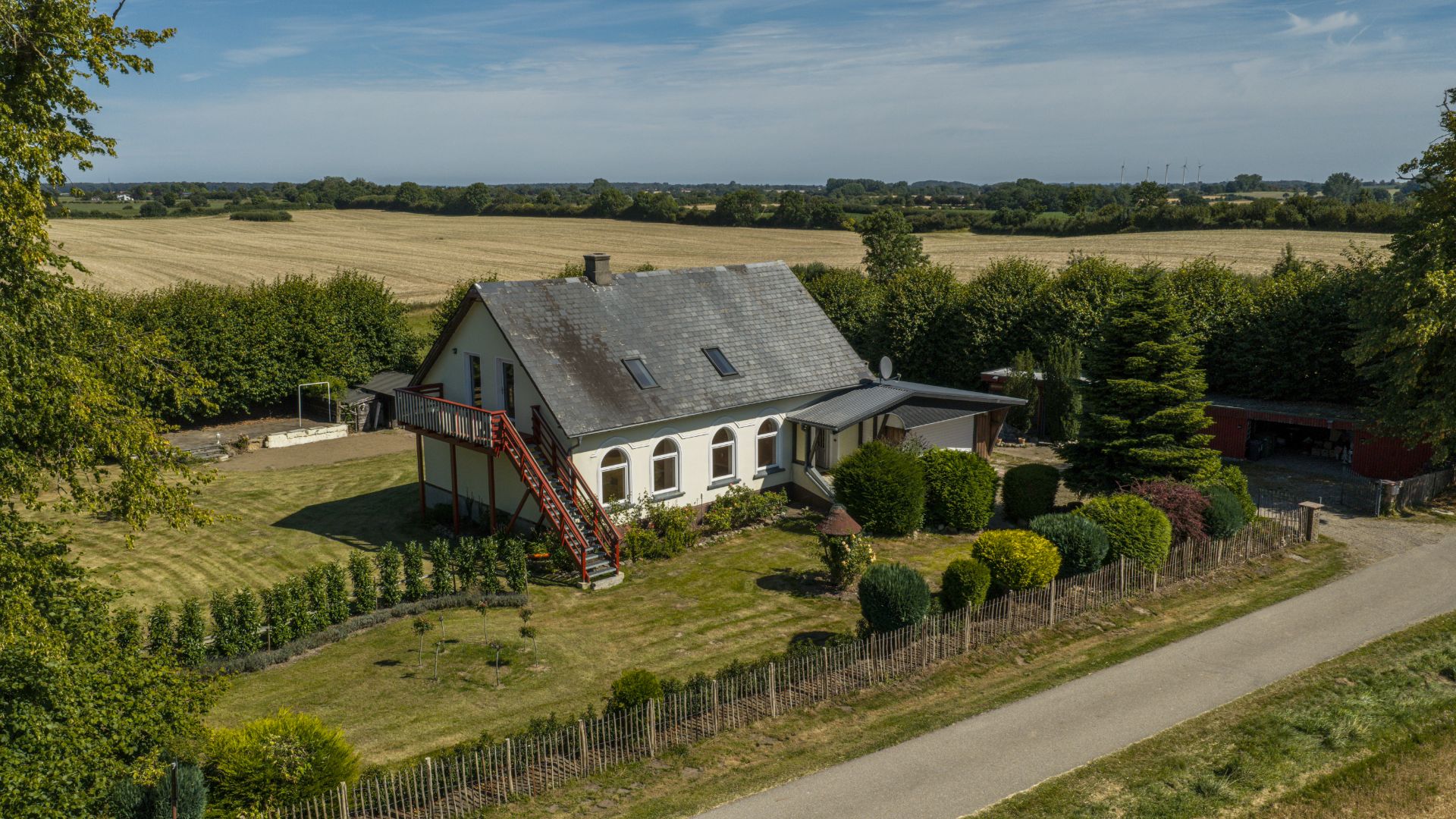 Einfamilienhaus mit großem Garten, roter Außentreppe und ländlicher Umgebung.