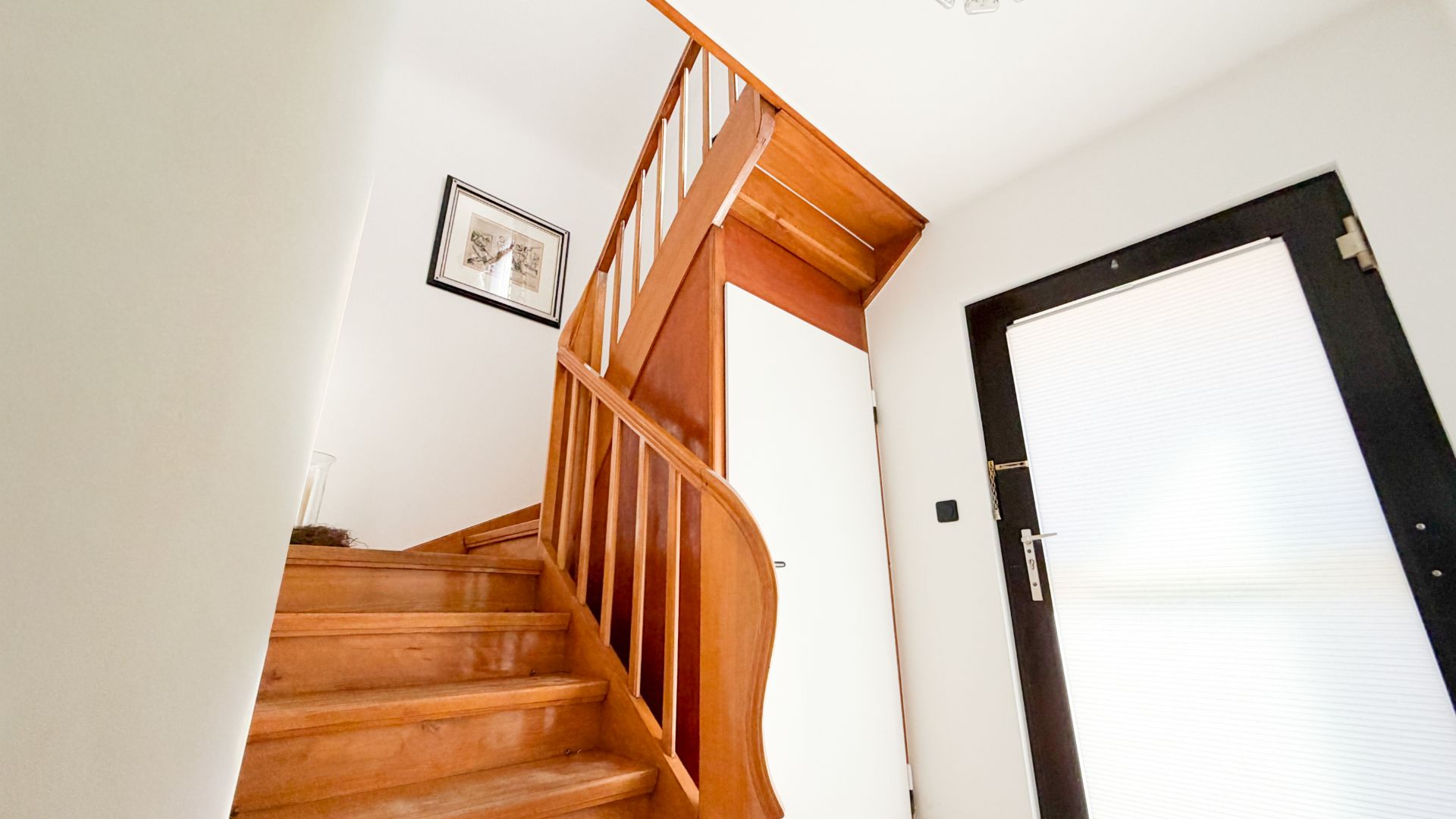 Holztreppe in einem Flur mit weißer Wand, Tür und einem gerahmten Bild an der Wand.