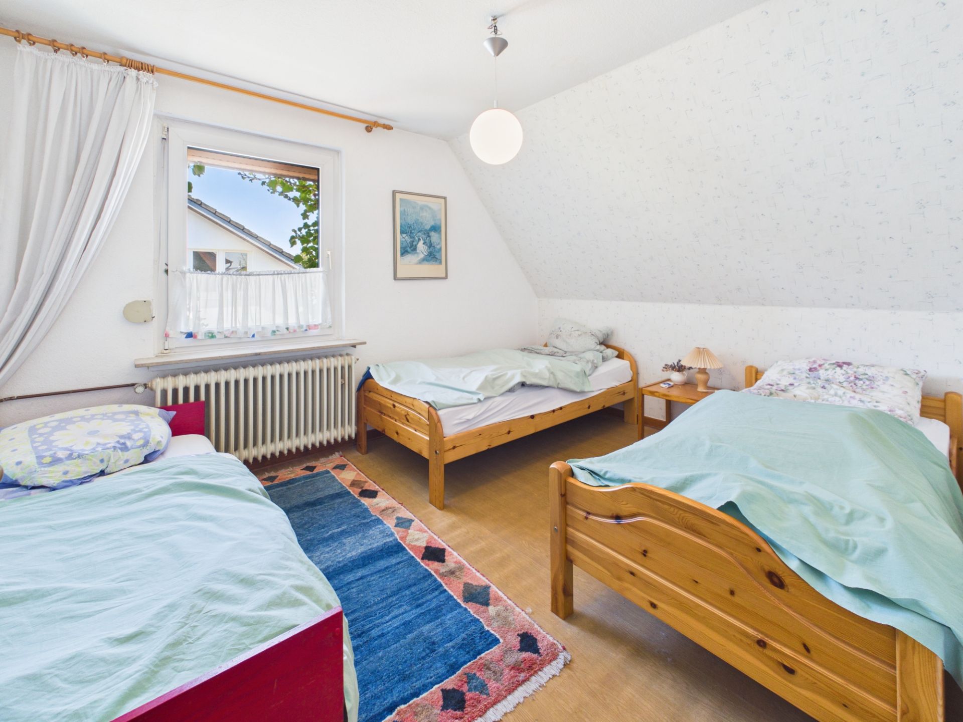 Helles Schlafzimmer mit drei Einzelbetten, Teppich und Fenster.