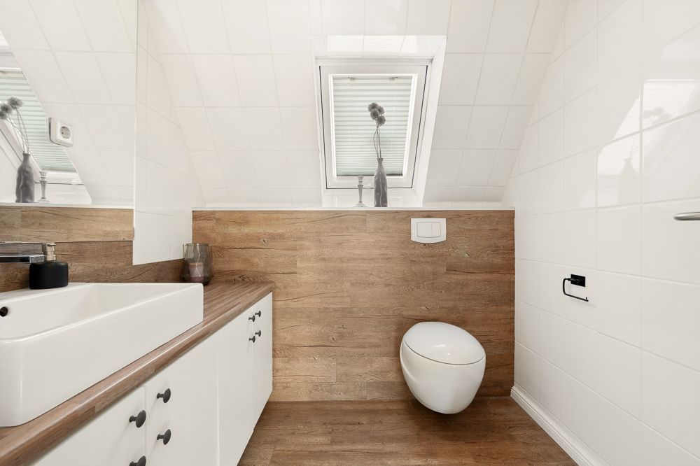 Modernes Badezimmer mit Hänge-WC, Waschbecken, Holzoptik und Dachfenster.