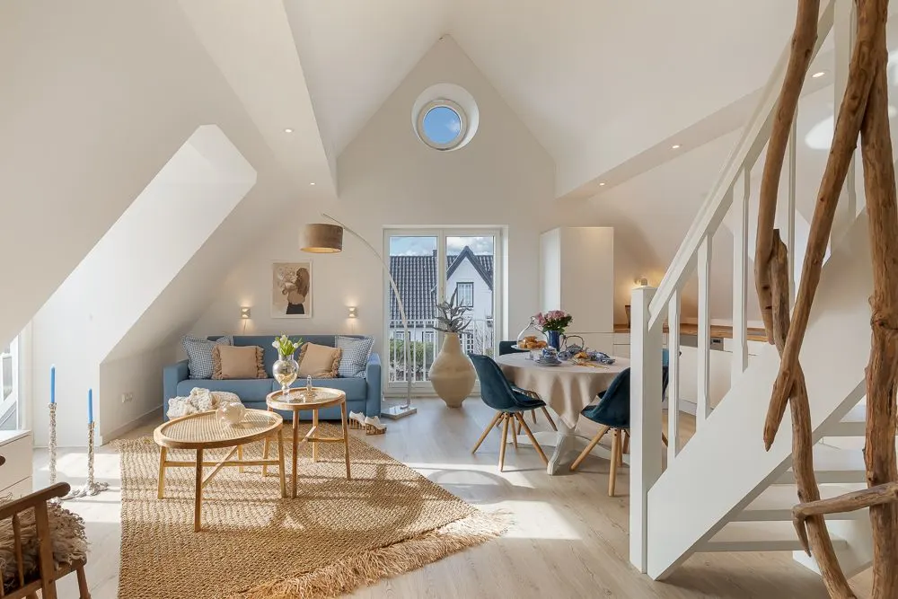 Helles Wohnzimmer mit blauem Sofa, Esstisch, runder Fensteröffnung und Treppe aus Holz.