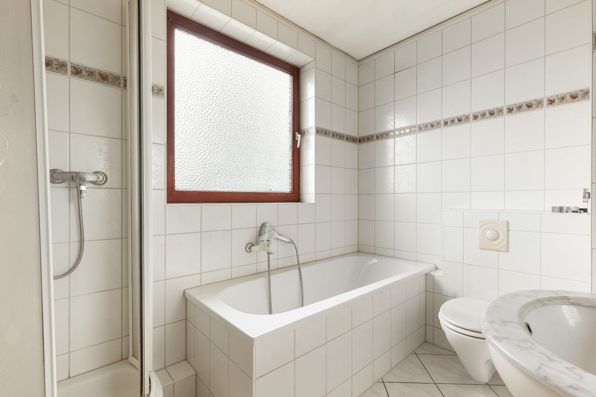 Helles Badezimmer mit Badewanne, Dusche, WC und Fenster.