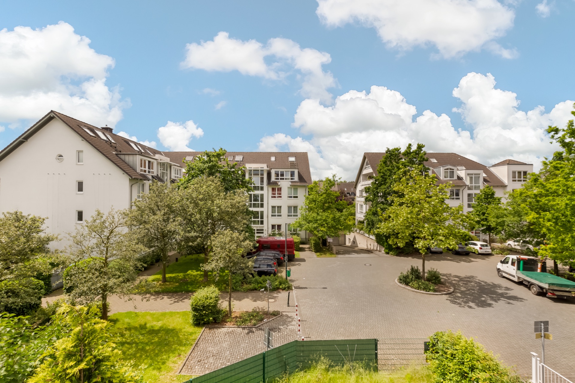 Mehrere Wohngebäude mit Bäumen, Parkplätzen und Autos an einem sonnigen Tag.