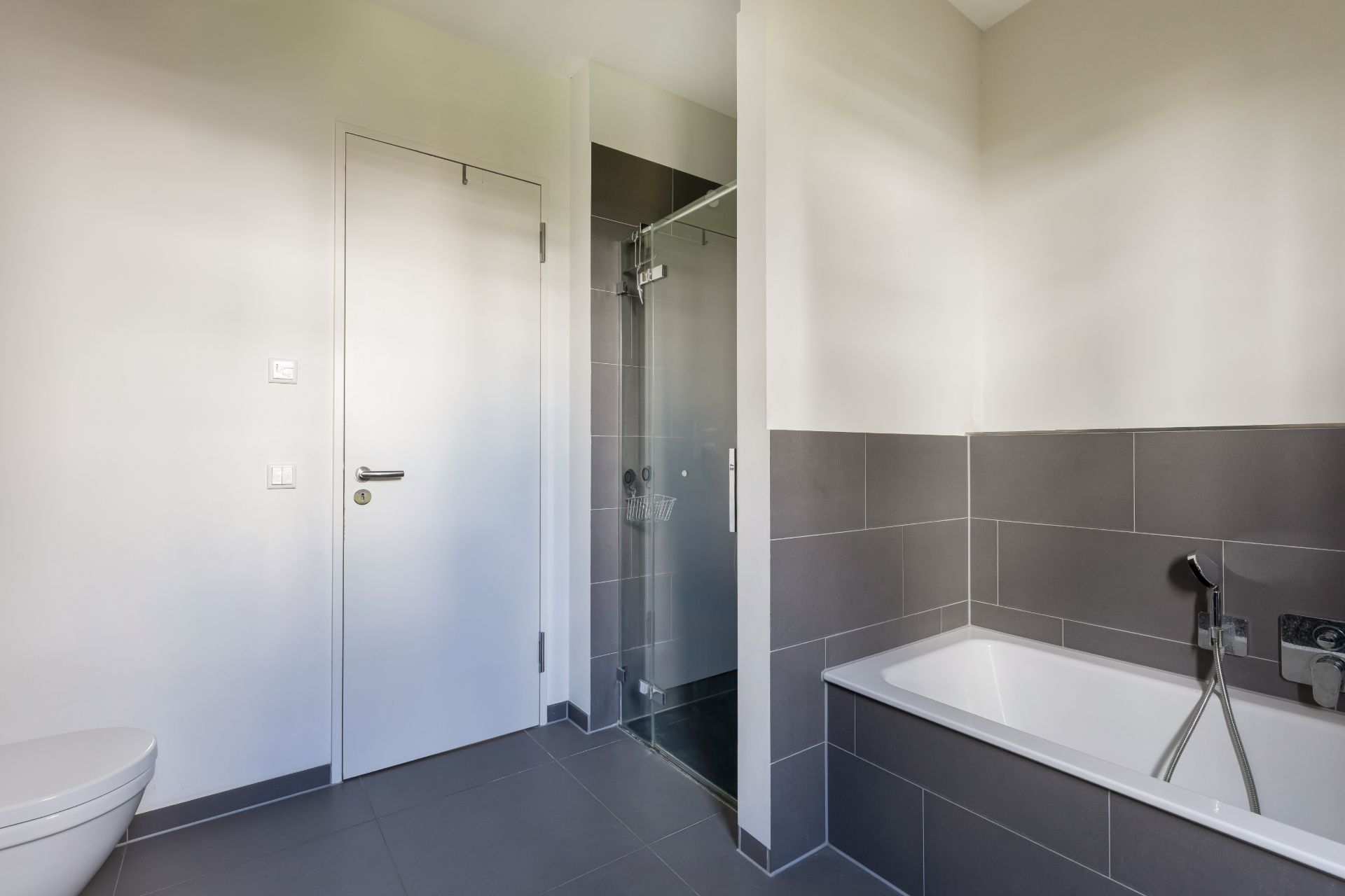 Modernes Badezimmer mit Badewanne, Dusche mit Glastür und weißer Tür.