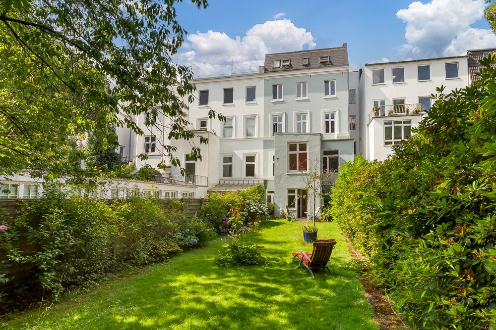 Grüner Garten mit Liegestuhl hinter einem mehrstöckigen Wohnhaus an einem sonnigen Tag.