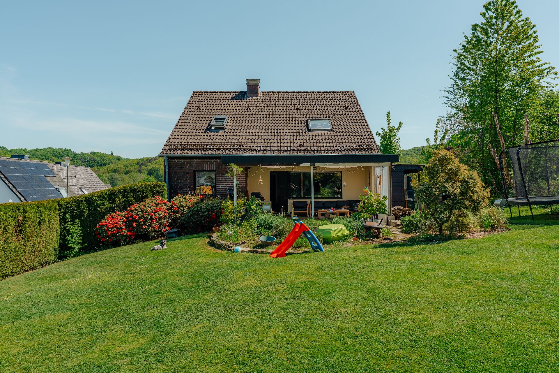 Ein Einfamilienhaus mit großem Garten, Rutsche, Trampolin und vielen Pflanzen.