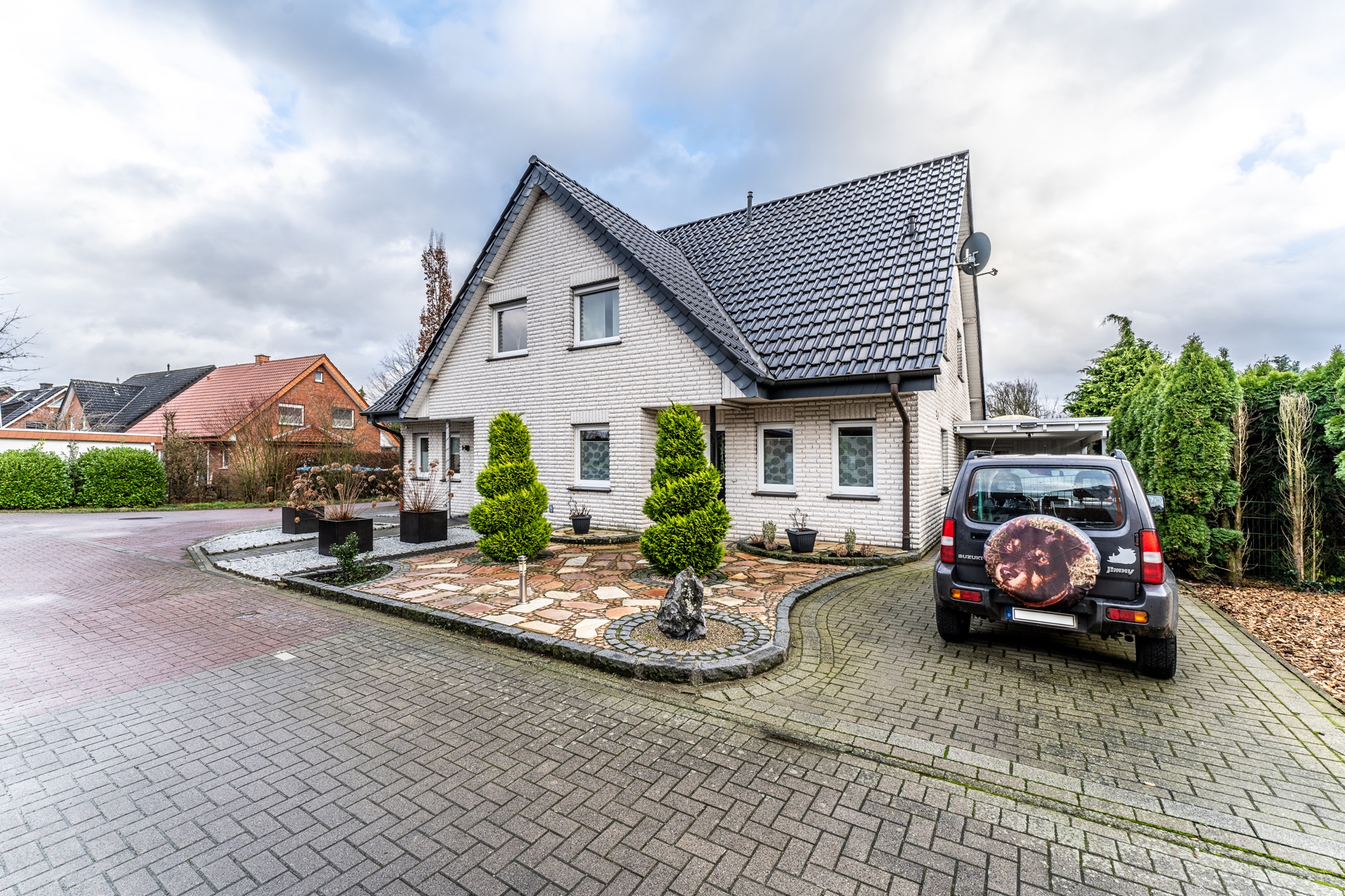 Modernes Einfamilienhaus mit gepflegtem Vorgarten und geparktem Auto auf gepflasterter Einfahrt.