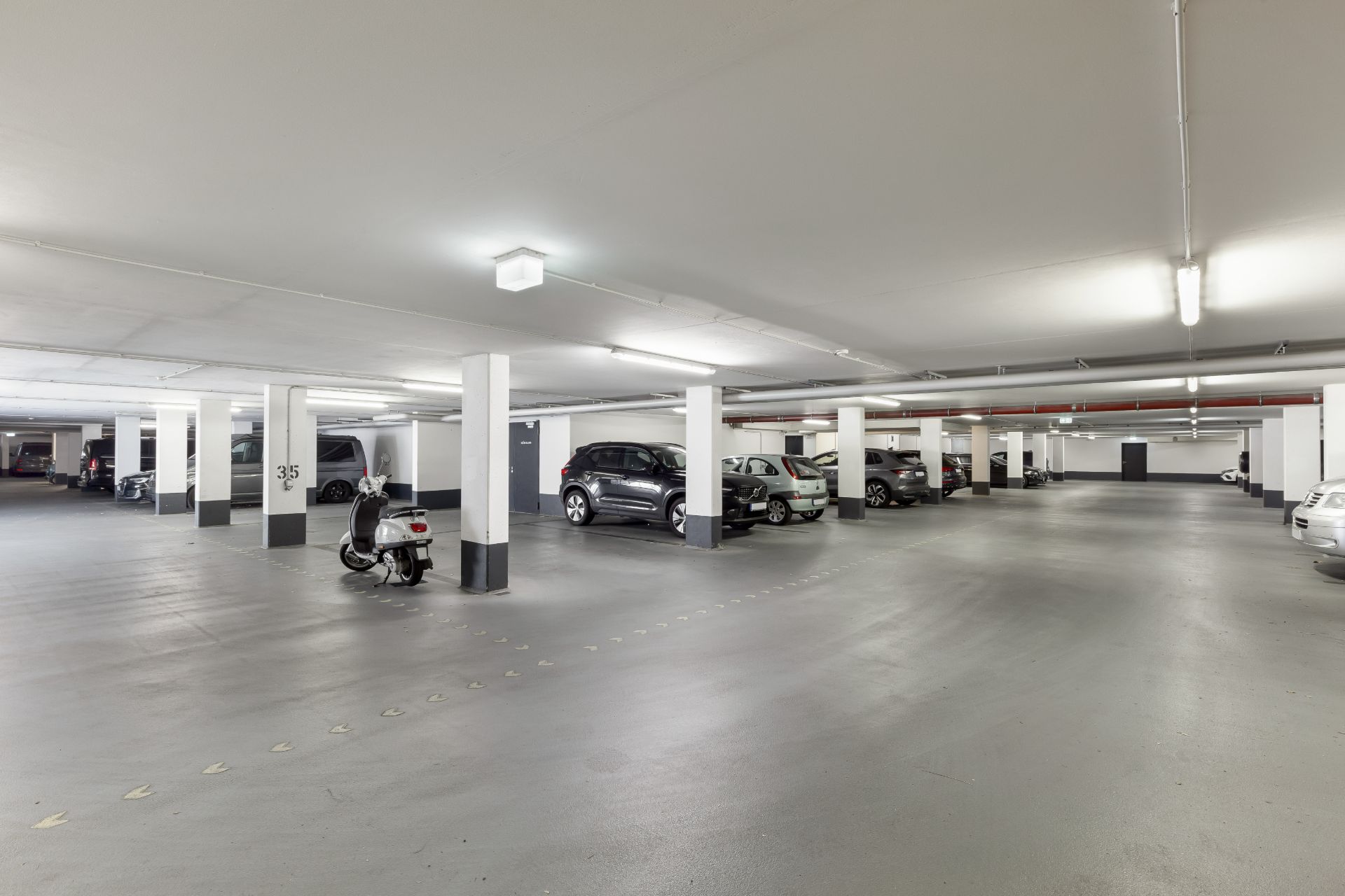 Helle, geräumige Tiefgarage mit mehreren geparkten Autos und einem Roller.