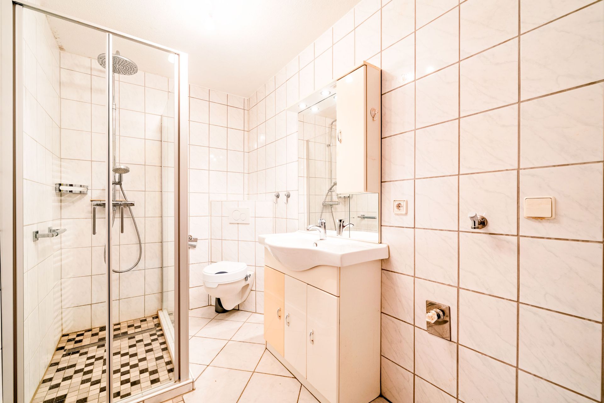 Modernes Badezimmer mit Dusche, WC und Waschbecken, alles mit weißen Fliesen.