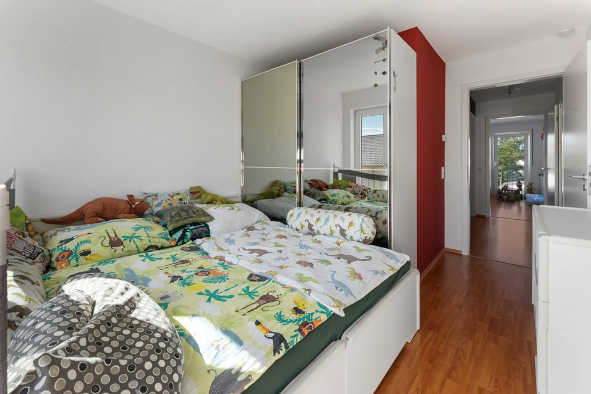 Kinderzimmer mit buntem Bett, Spiegel-Schrank und Blick auf einen Flur mit Holzboden.
