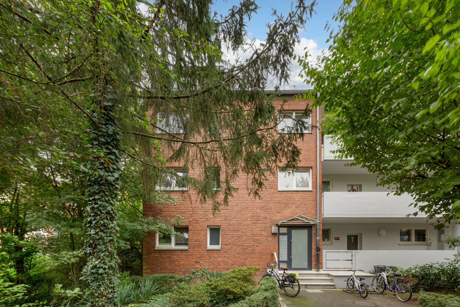 Wohnhaus mit roter Fassade, umgeben von Bäumen, mehrere Fahrräder vor dem Eingang.