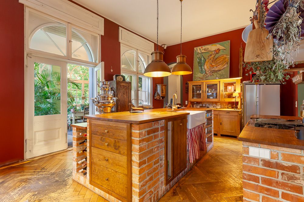 Große, helle Küche mit roten Wänden, Holzmöbeln, Kücheninsel und Blick auf eine Terrasse mit Pflanzen.