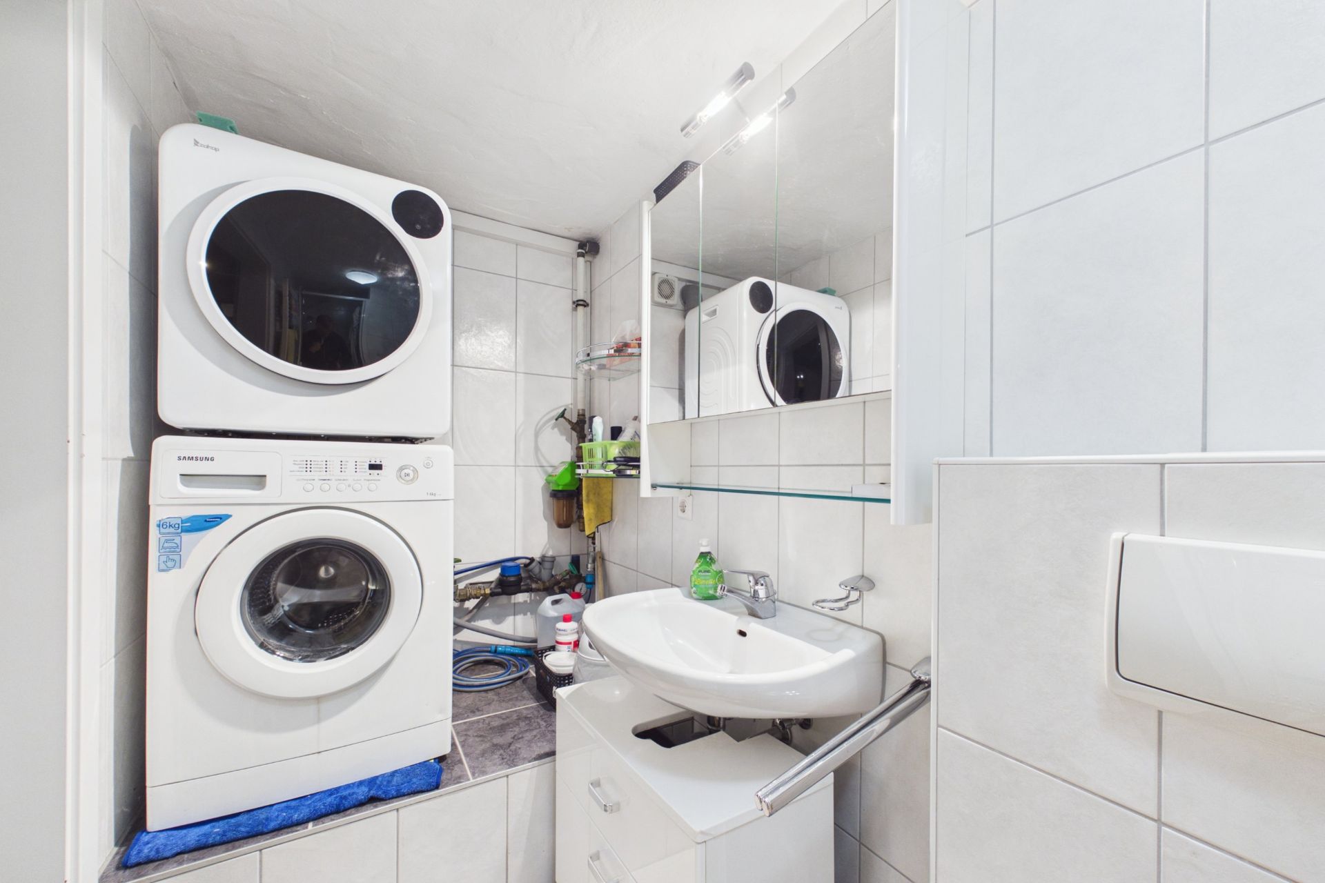 Kleines Badezimmer mit Waschbecken, Spiegel und gestapelter Waschmaschine und Trockner.