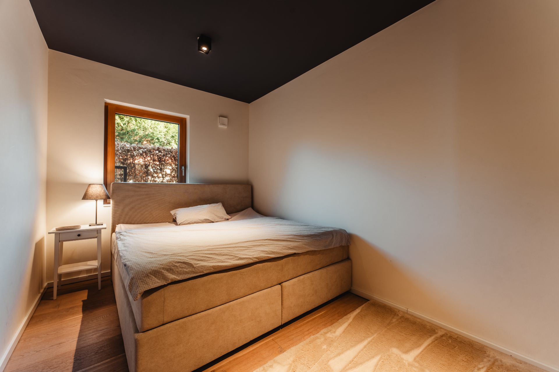Schlafzimmer mit Doppelbett, Nachttisch mit Lampe und Fenster mit Blick ins Grüne.