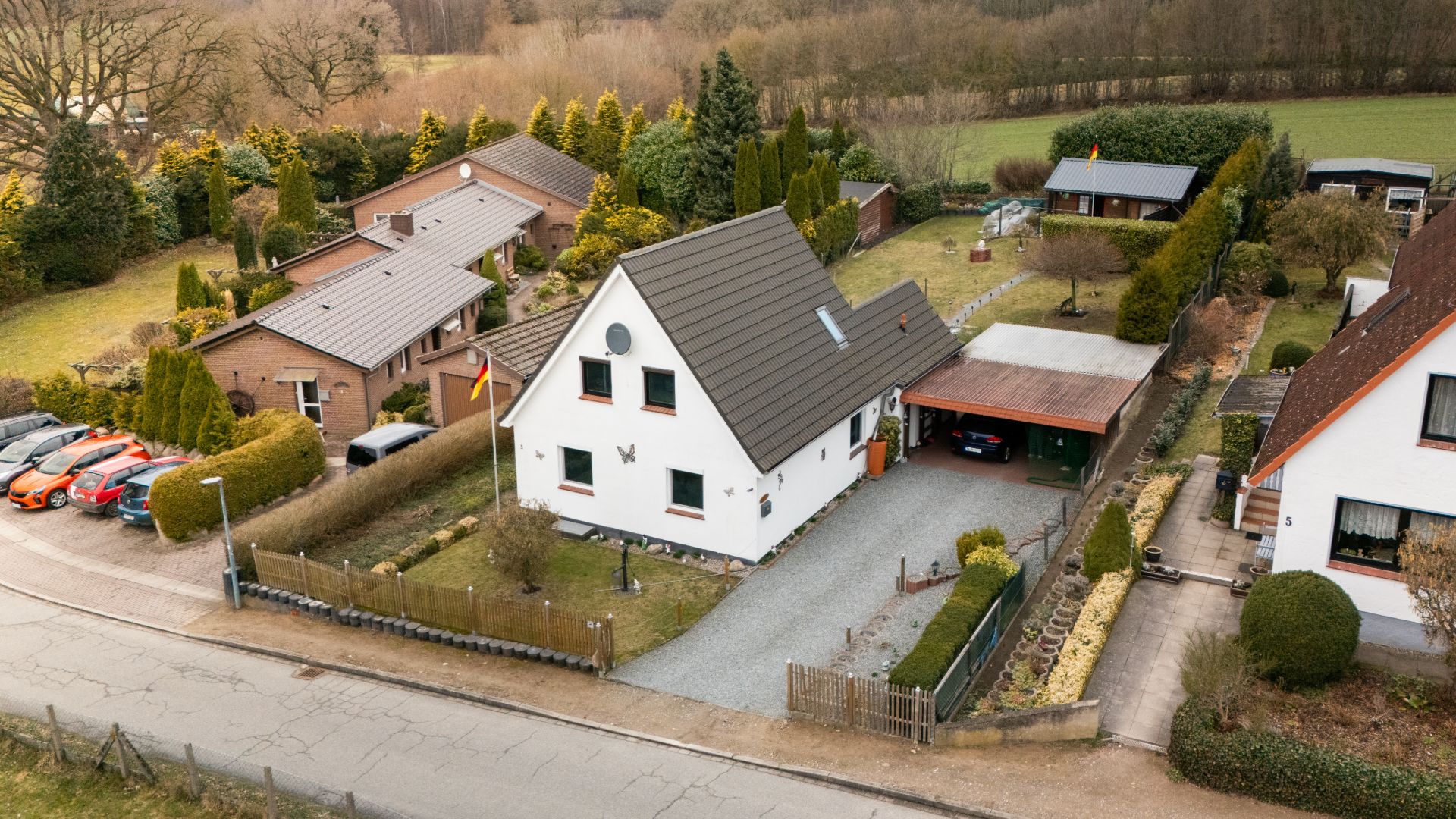Luftaufnahme eines weißen Einfamilienhauses mit Garten, Auffahrt und Carport in ruhiger Wohngegend.