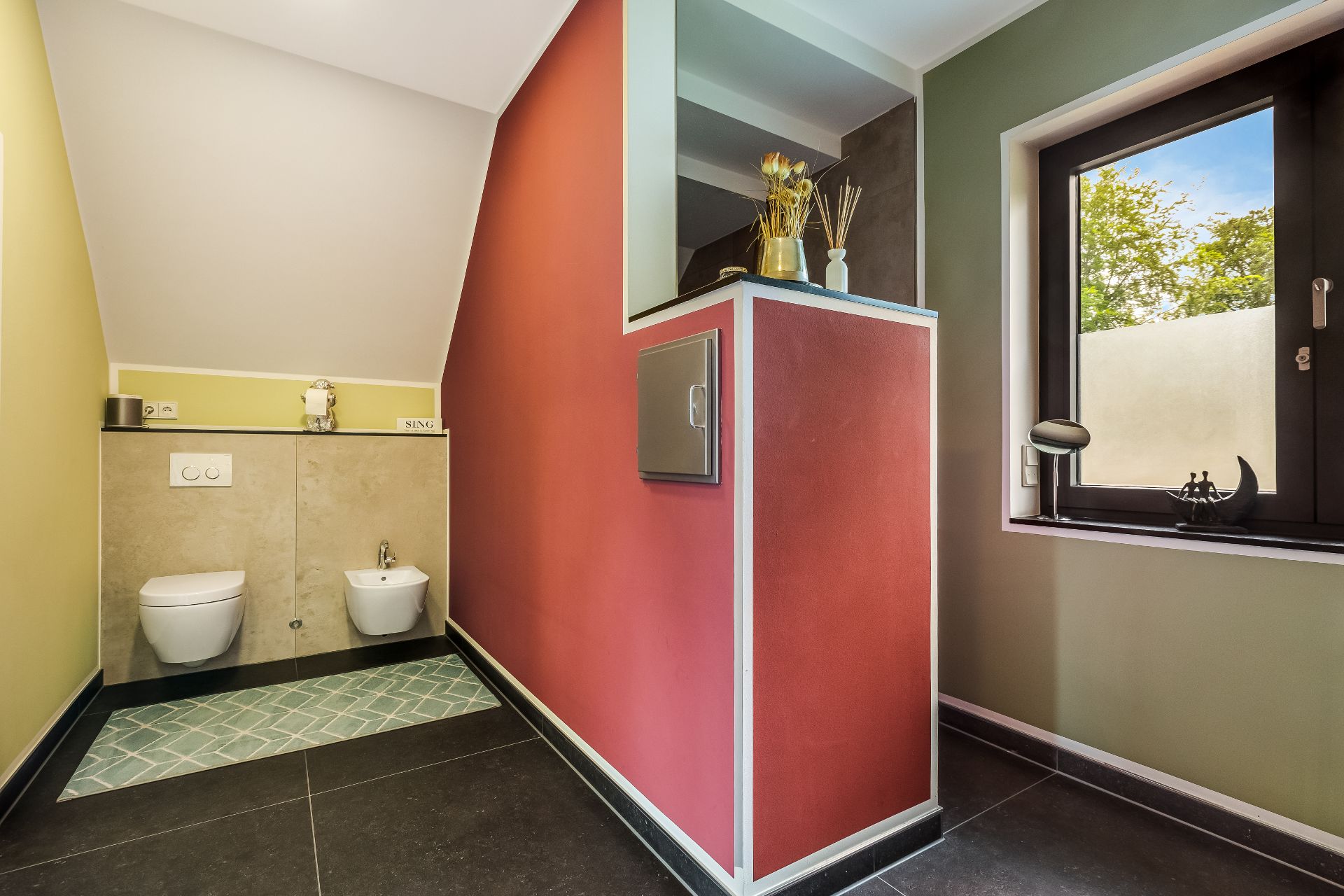 Modernes Bad mit Hänge-WC, Bidet und Fenster. Der Raum hat farbige Wände und Dekoration.