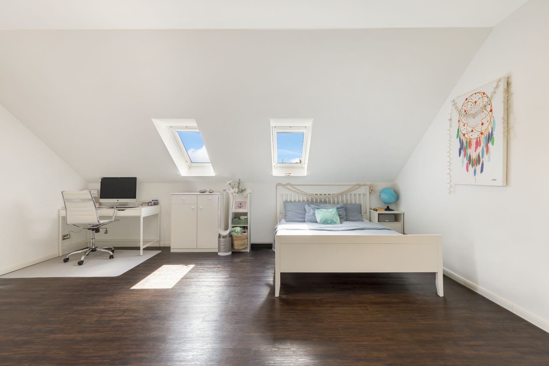 Helles Schlafzimmer mit Schreibtisch, Bett und zwei Dachfenstern unter einer Dachschräge.