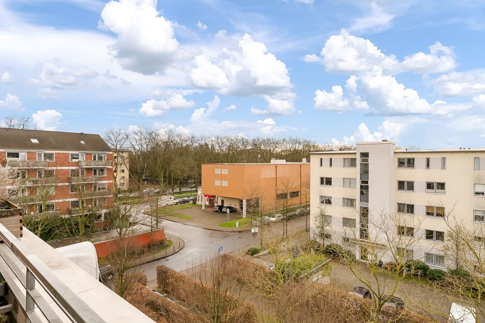 Aussicht auf Wohngebäude, Straße und Bäume unter blauem Himmel mit Wolken.