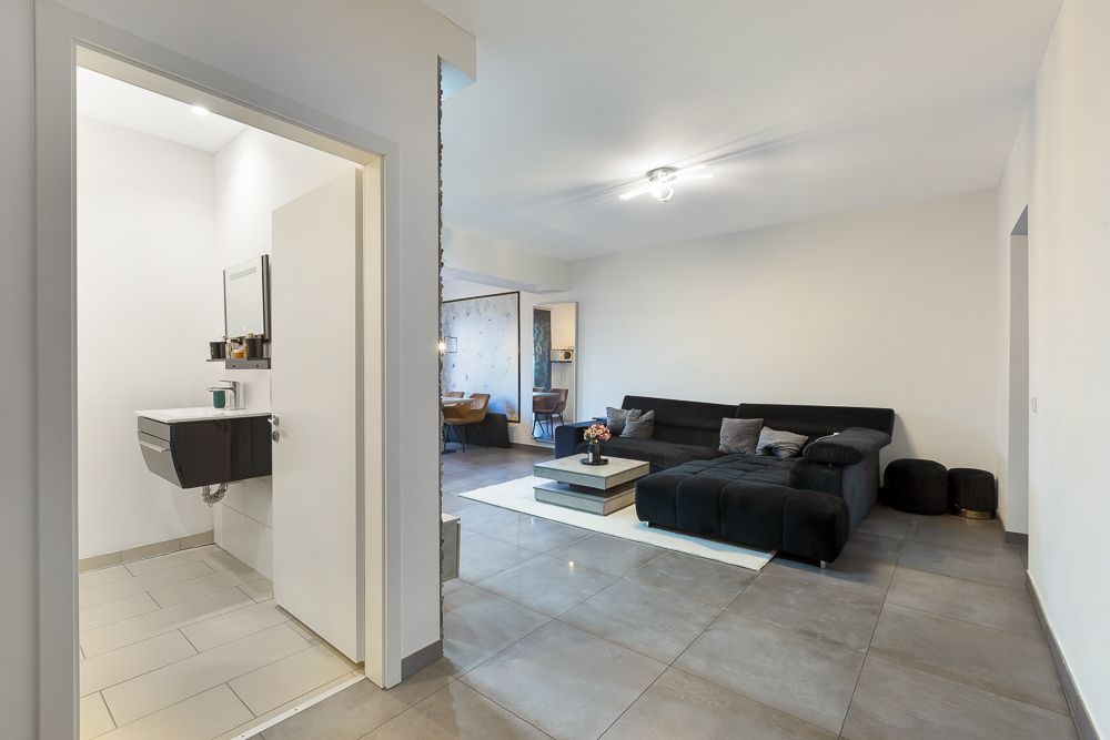 Modernes Wohnzimmer mit schwarzem Sofa, Couchtisch und Blick in ein kleines, helles Bad.
