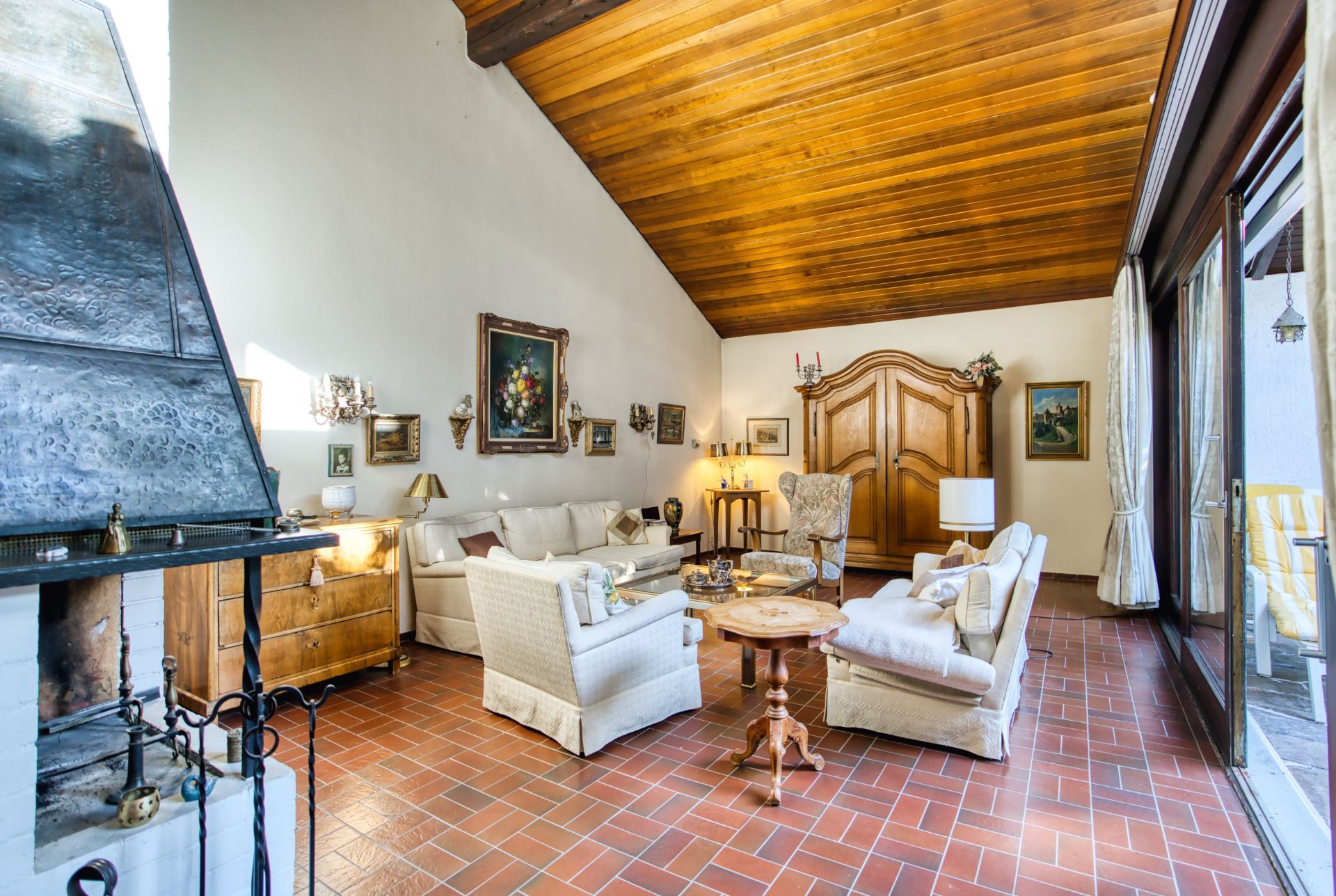 Helles Wohnzimmer mit Kamin, Holzbalkendecke, weißen Sofas und großen Fenstern.