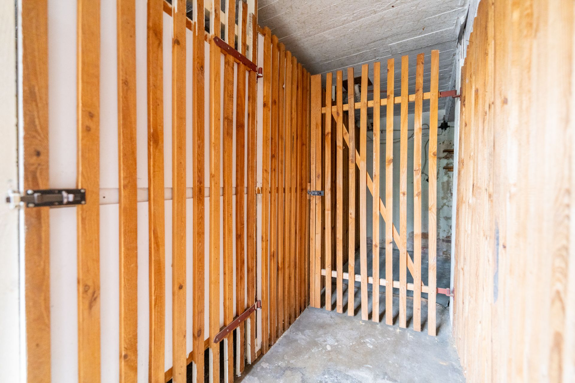 Kellerabteil mit Holzgitterwänden und Betonboden in einem Wohngebäude.