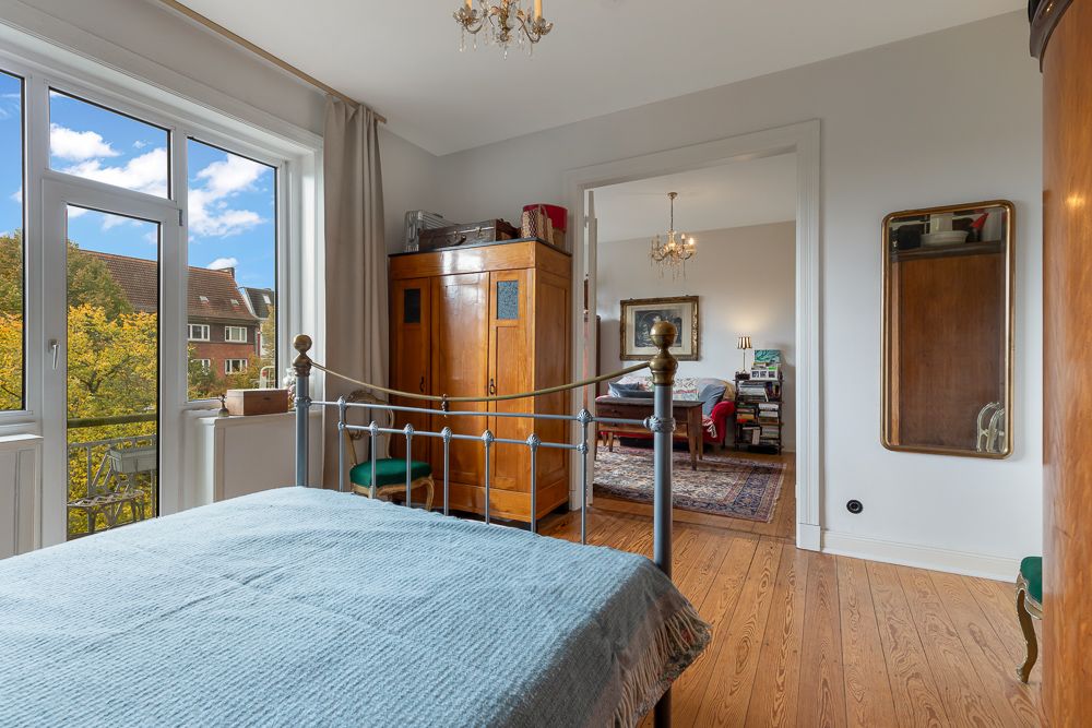 Schlafzimmer mit Metallbett, Holzboden, großem Fenster und Blick in ein weiteres Zimmer.
