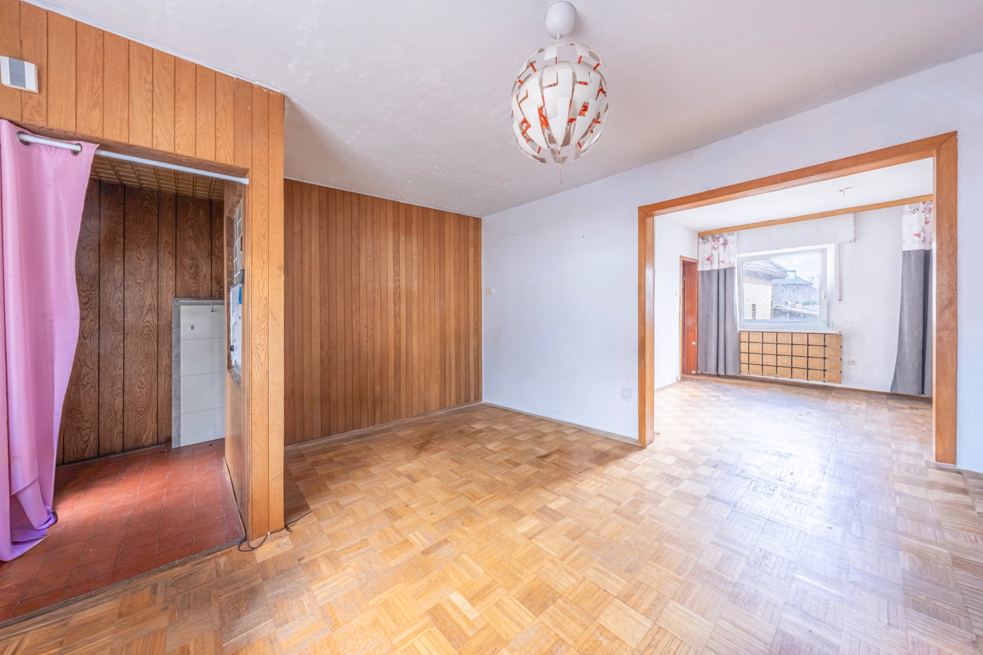 Helles Wohnzimmer mit Holzverkleidung, Parkettboden und Blick in ein weiteres Zimmer.