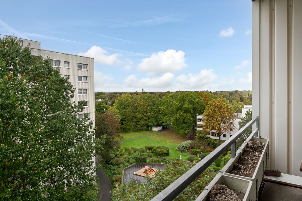 Blick vom Balkon auf Grünfläche mit Spielplatz und Wohngebäude im Hintergrund.