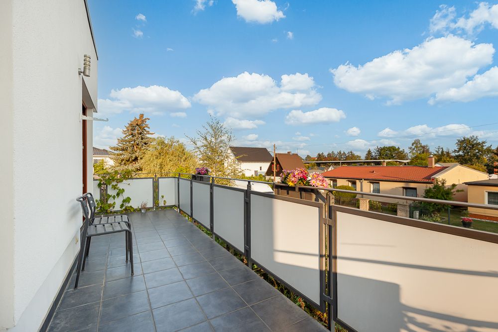 Geräumiger Balkon mit zwei Stühlen, Blick auf Nachbarhäuser und blauen Himmel mit Wolken.