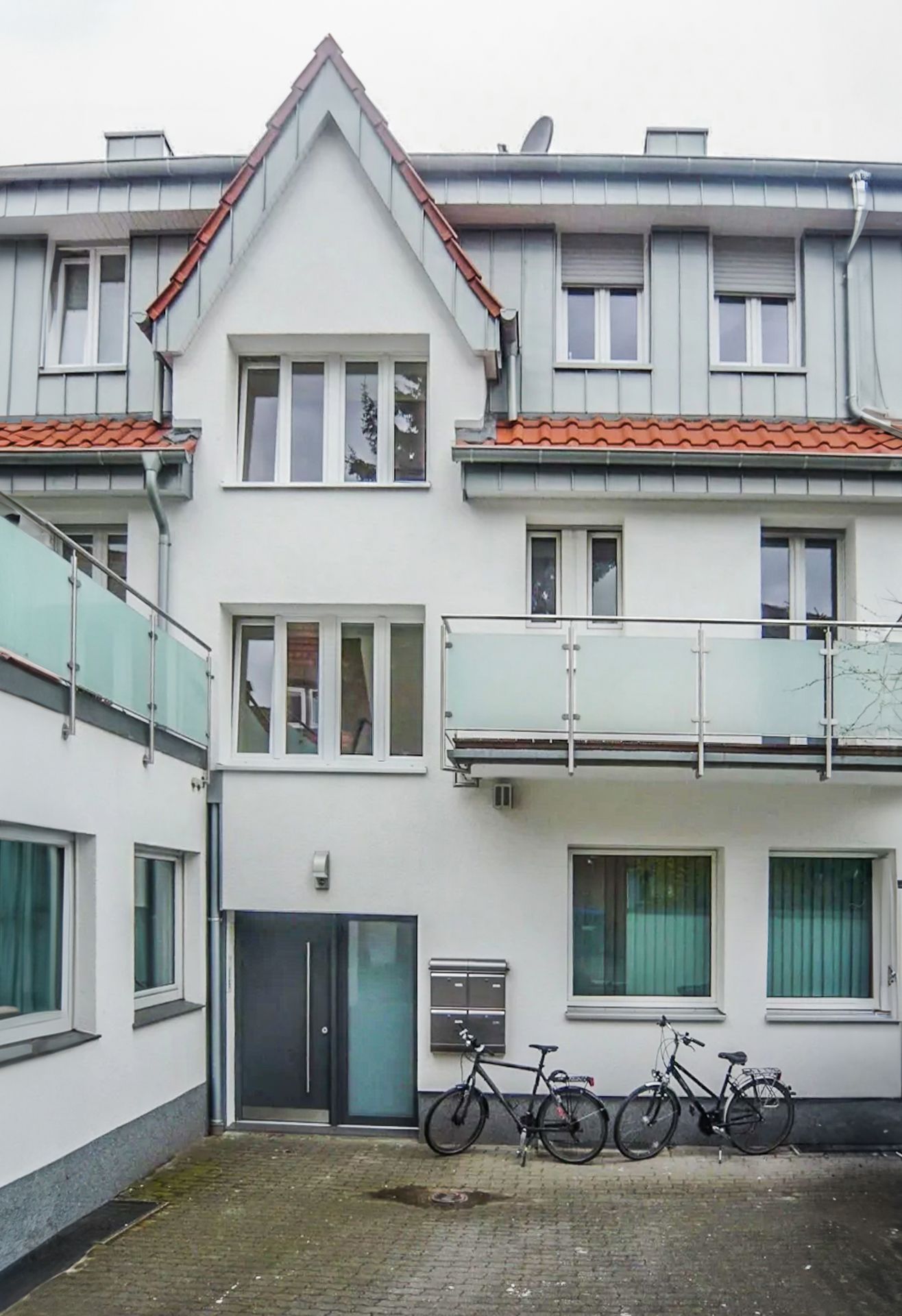 Mehrfamilienhaus mit weißen Wänden, Balkonen und zwei abgestellten Fahrrädern im Hof.