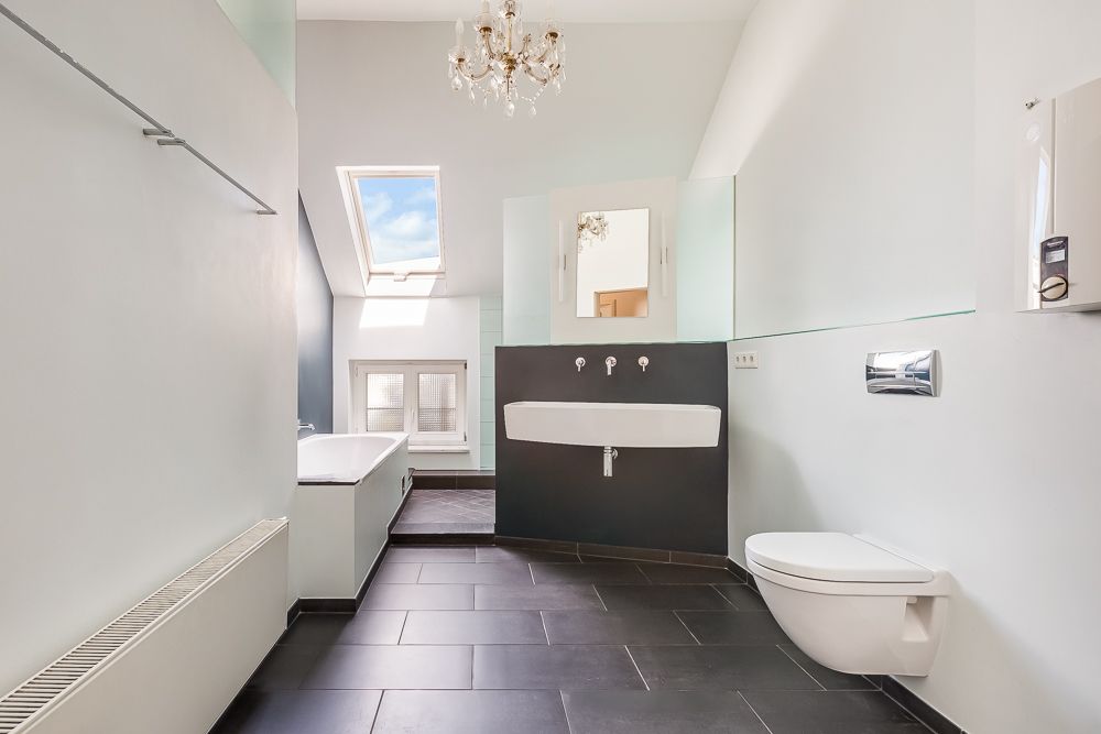 Modernes Badezimmer mit Hängetoilette, Waschbecken, Badewanne und Dachfenster.