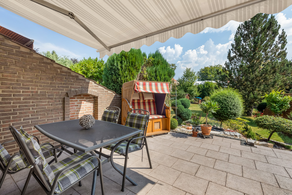 Terrasse mit Tisch, Stühlen, Strandkorb und Markise, Blick auf gepflegten Garten.
