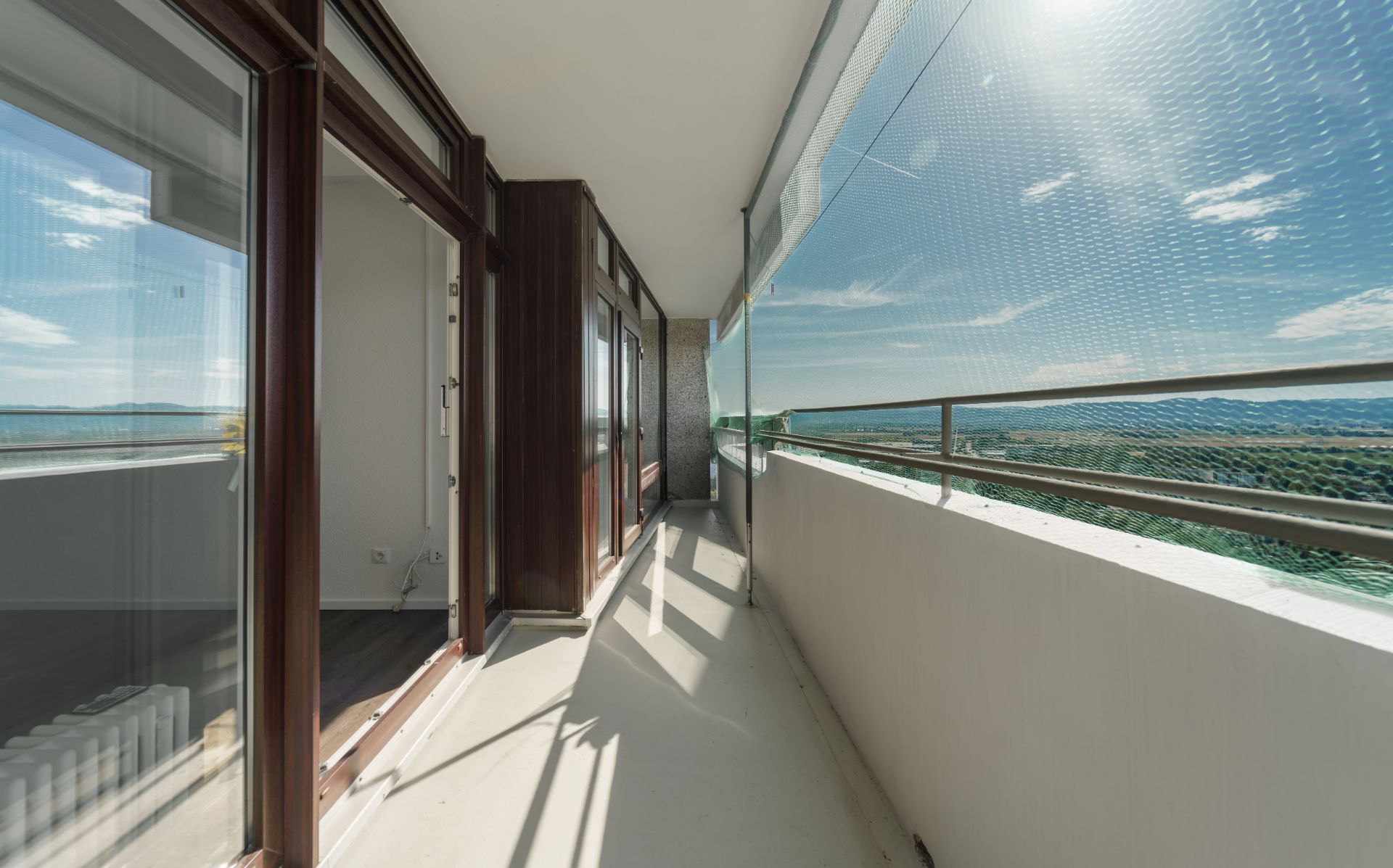 Langer Balkon mit Glasfront, Blick ins Grüne und Schutznetz an der Brüstung.