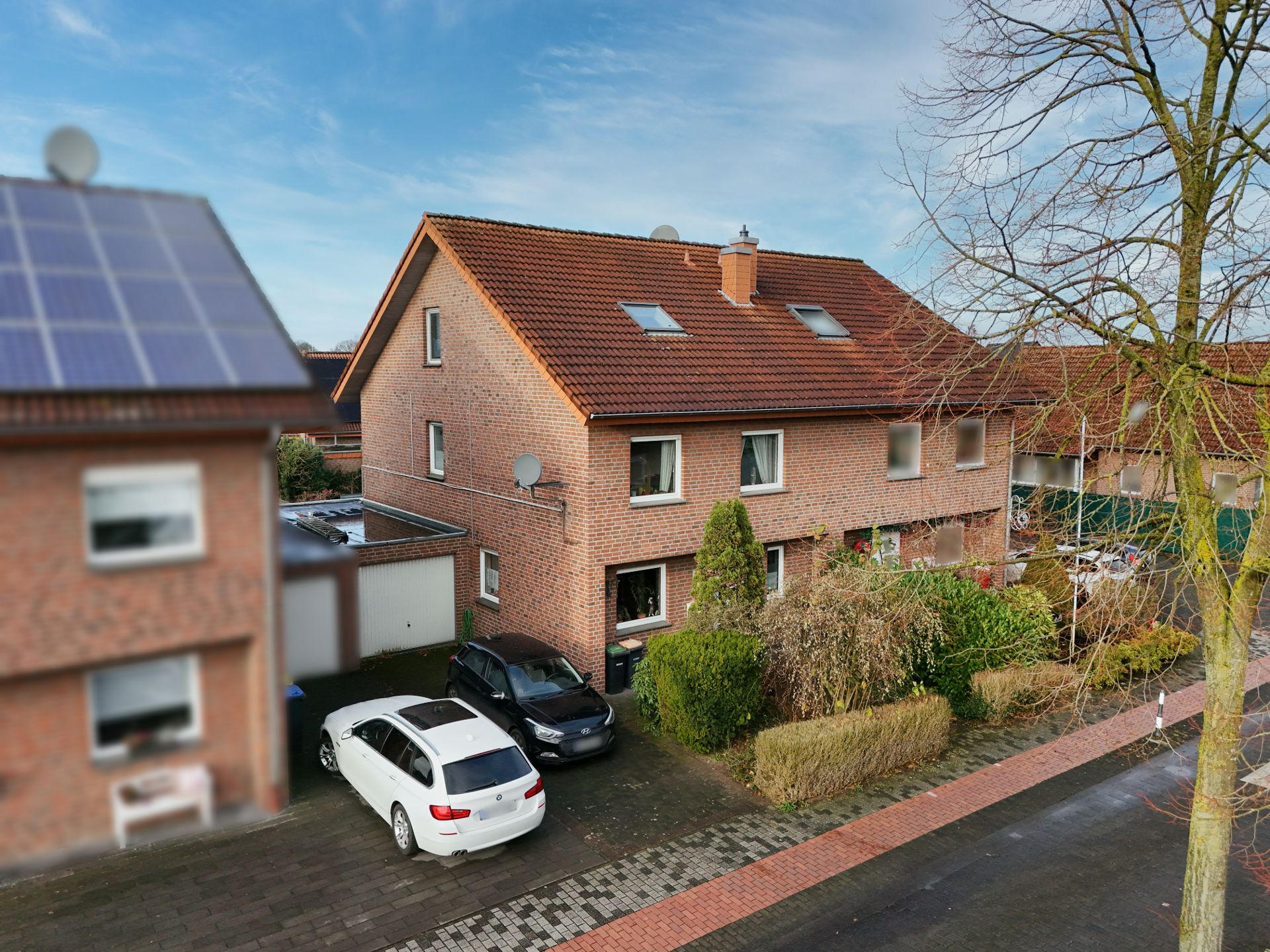Doppelhaushälfte aus rotem Klinker mit zwei geparkten Autos und Vorgarten.