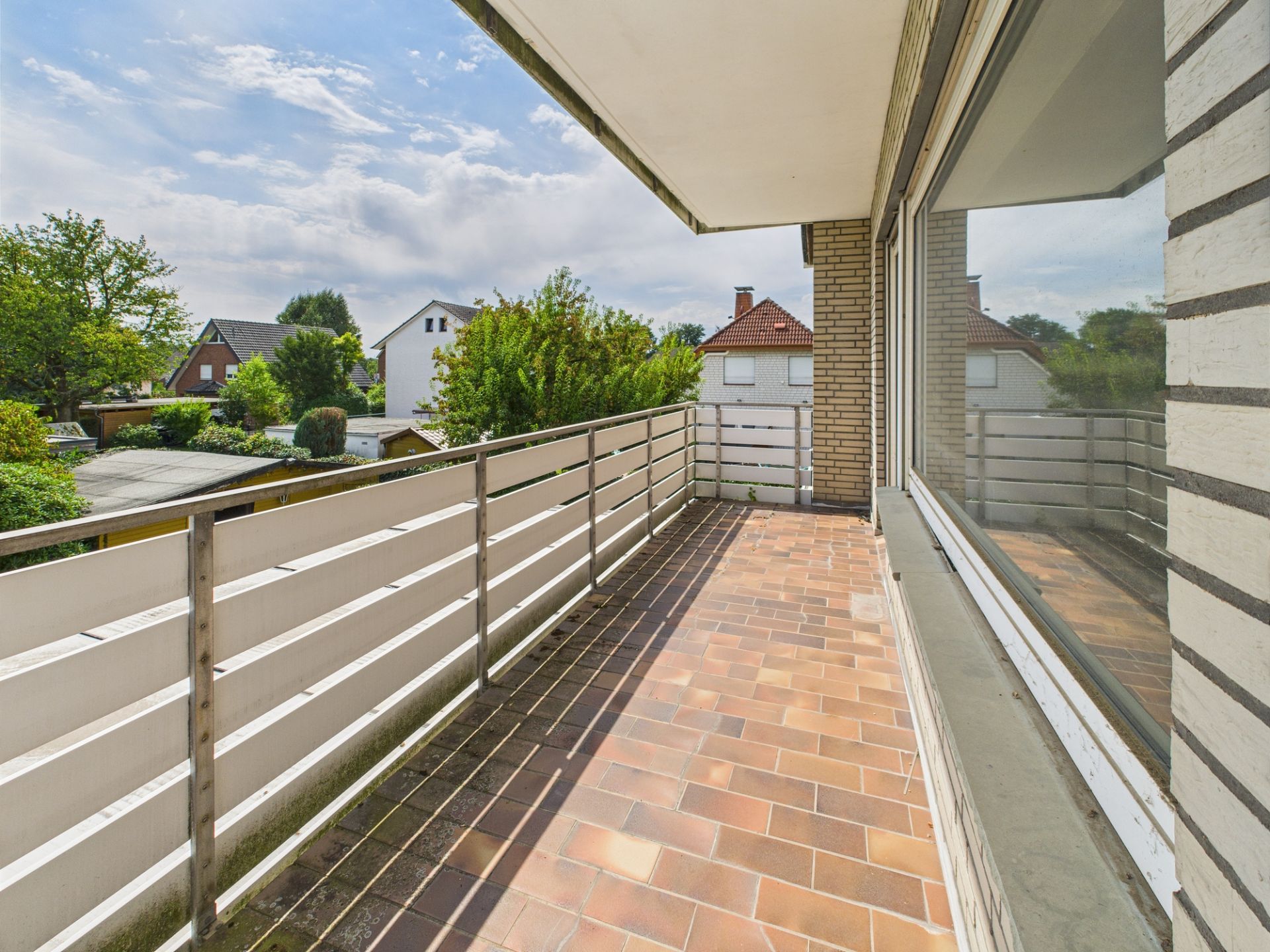 Geräumiger Balkon mit Metallgeländer und Fliesenboden, Blick auf Nachbarhäuser und Bäume.