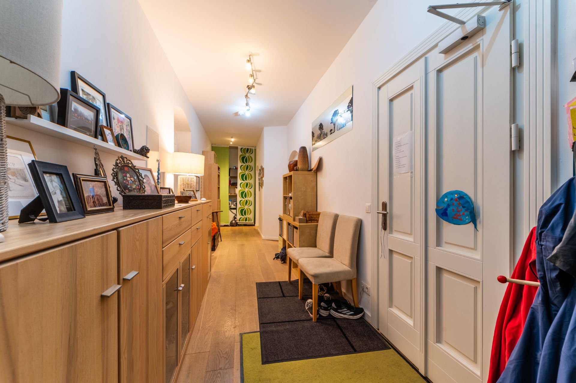 Heller Flur mit Holzmöbeln, Fotos, zwei Stühlen, Garderobe und Schuhen auf dem Boden.