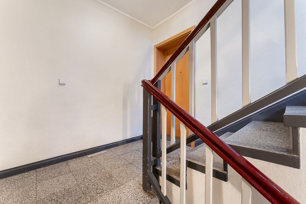 Treppenhaus mit Geländer, Tür und hellen Wänden in einem Wohnhaus.