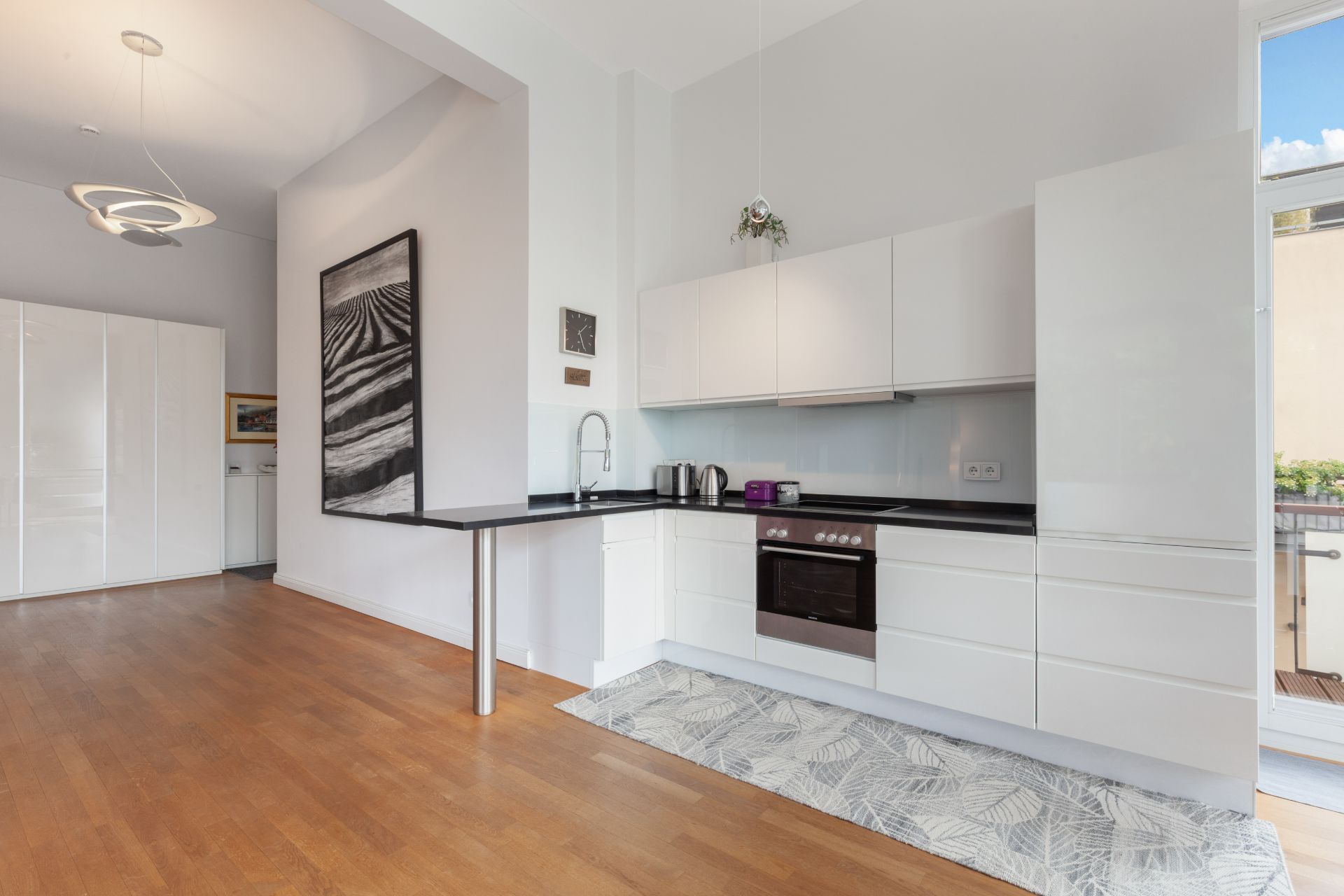 Moderne weiße Einbauküche mit Elektroherd, Holzfußboden und großem Fenster.