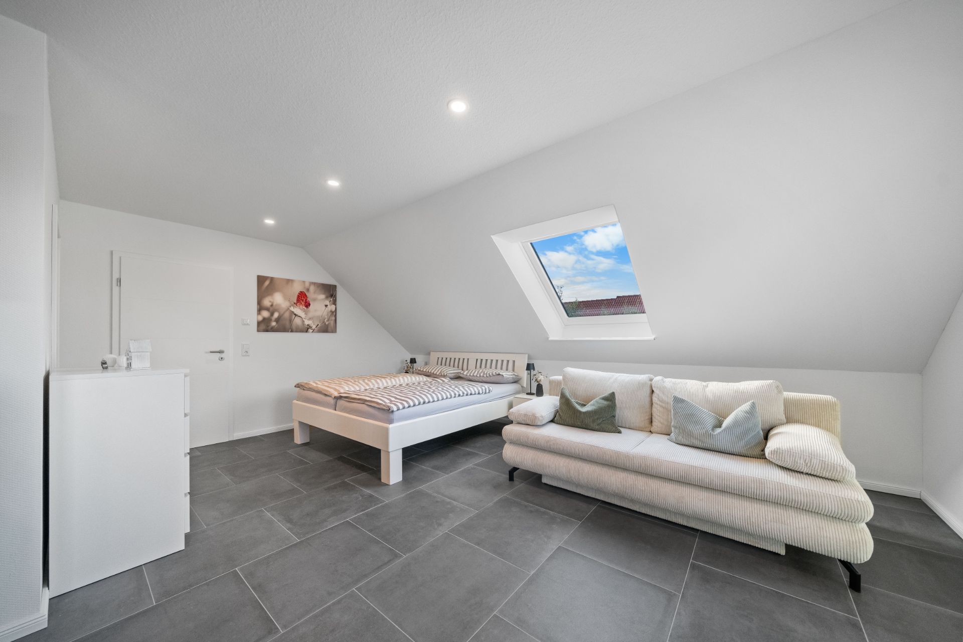 Helles Schlafzimmer mit Bett, Sofa und Dachfenster in modernem Design.
