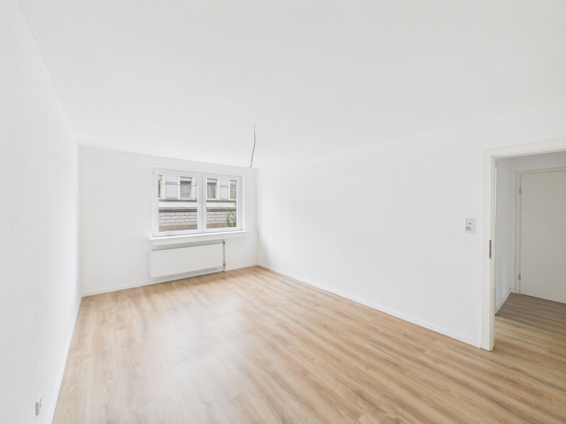 Heller, leerer Raum mit Holzfußboden, weiß gestrichenen Wänden und Fenster.