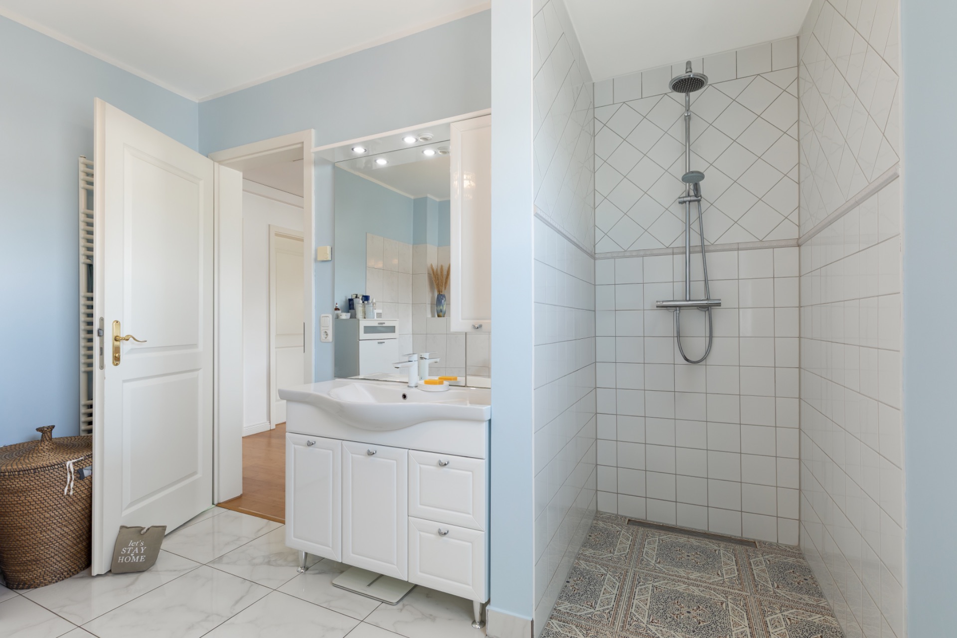 Modernes Badezimmer mit begehbarer Dusche, weißem Waschbecken und offen stehender Tür.