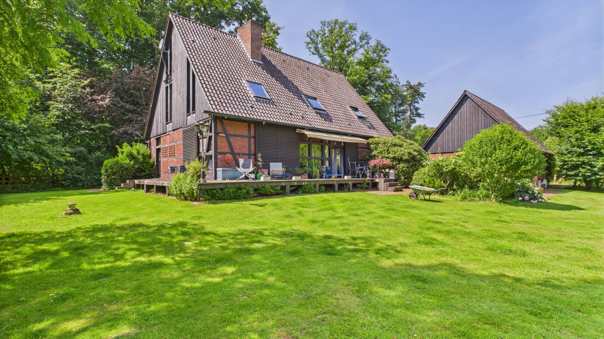 Ein Haus mit schrägem Dach, Terrasse und großem, grünen Garten bei sonnigem Wetter.