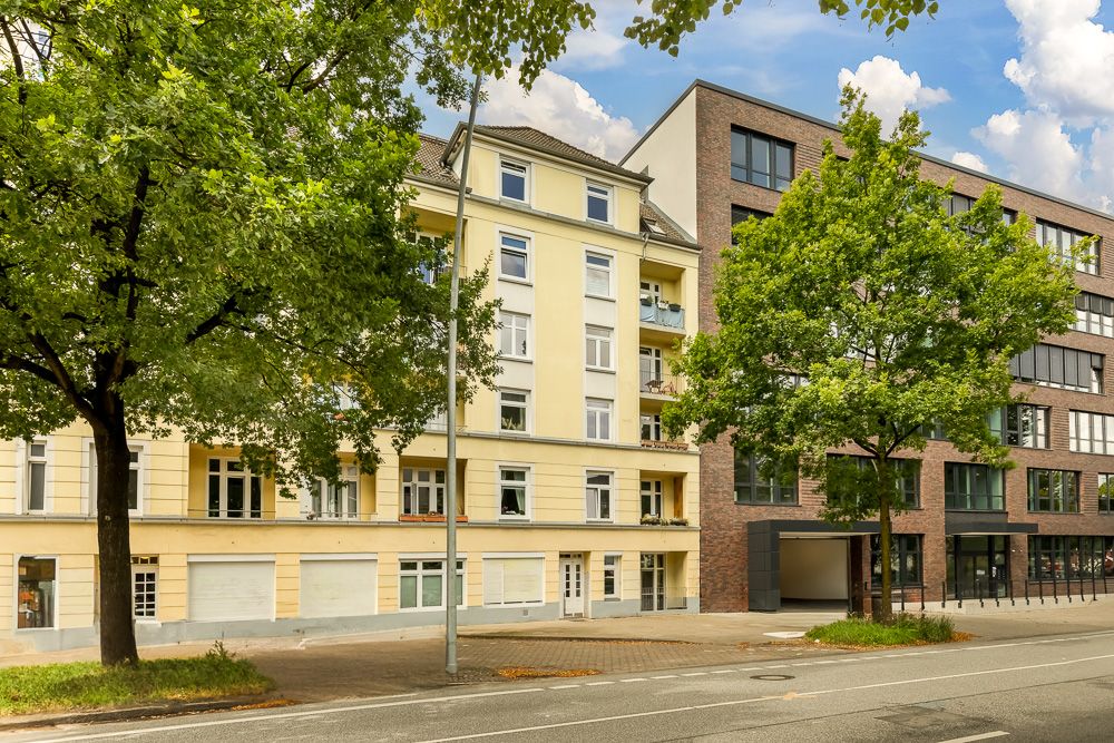 Mehrgeschossiges Wohnhaus mit gelber Fassade, Bäumen und Gehweg davor.