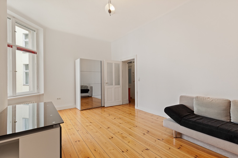 Helles Wohnzimmer mit Holzboden, Sofa, Spiegelschrank und großem Fenster.