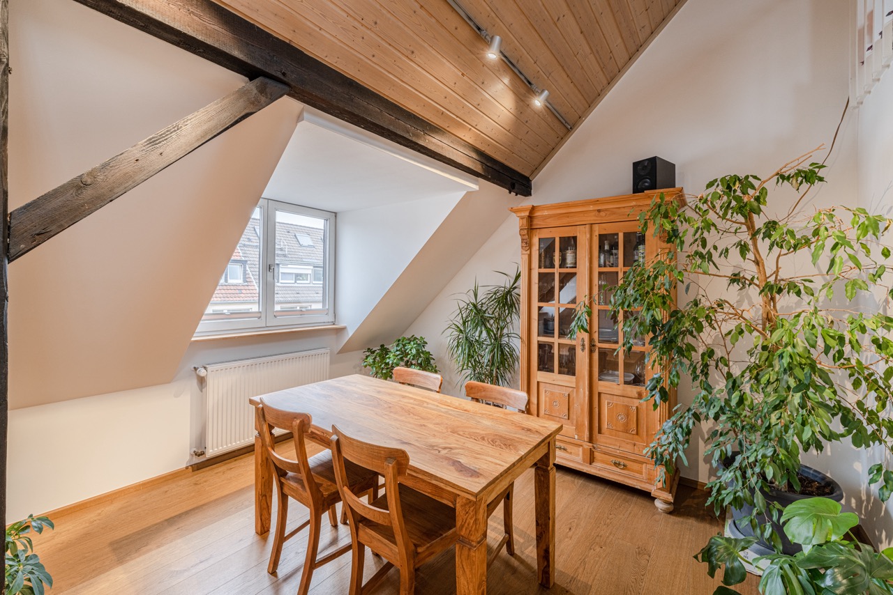 Essbereich mit Holztisch, vier Stühlen, Vitrine und mehreren Pflanzen unter Dachschräge.