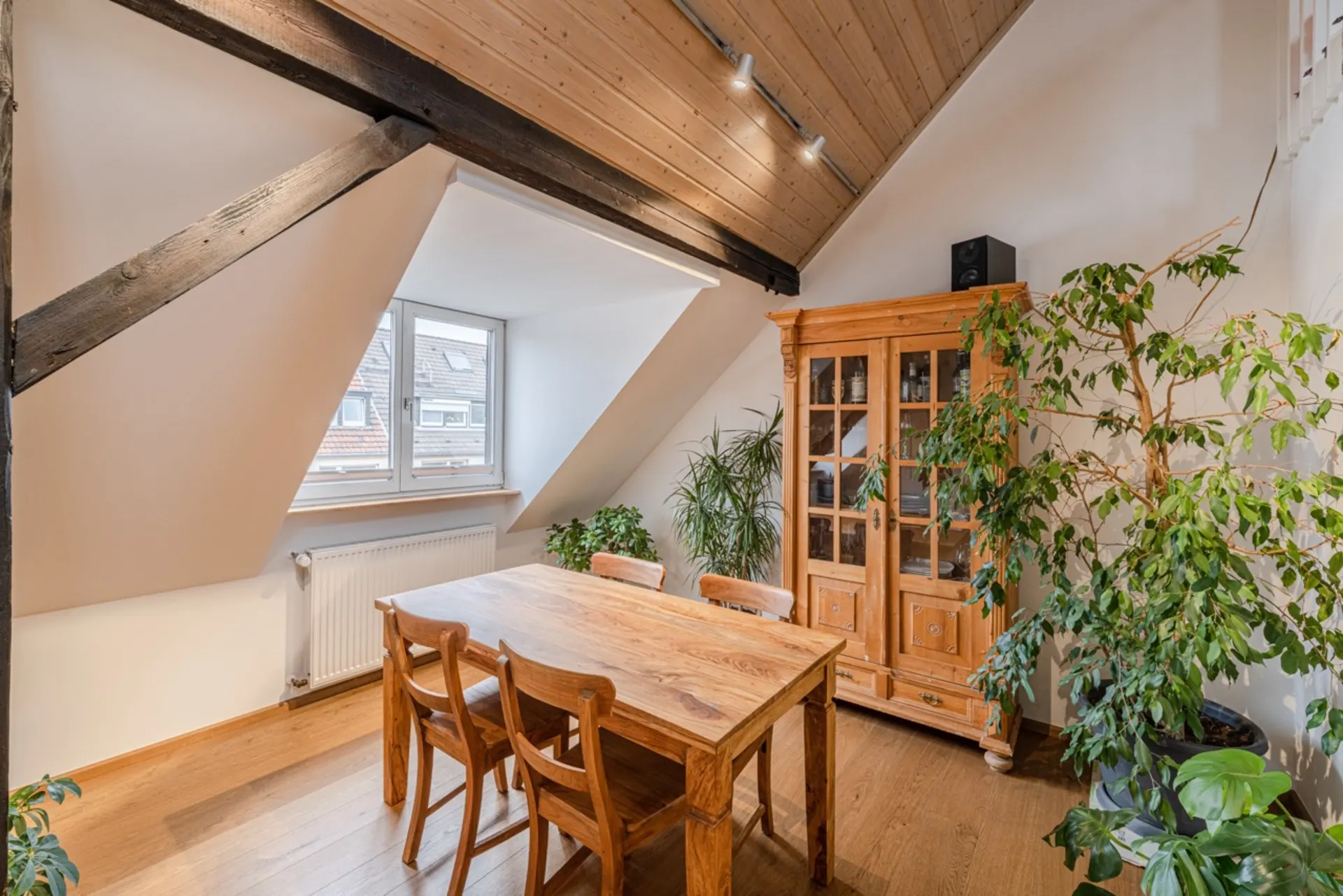 Essbereich mit Holztisch, vier Stühlen, Vitrine und mehreren Pflanzen unter Dachschräge.