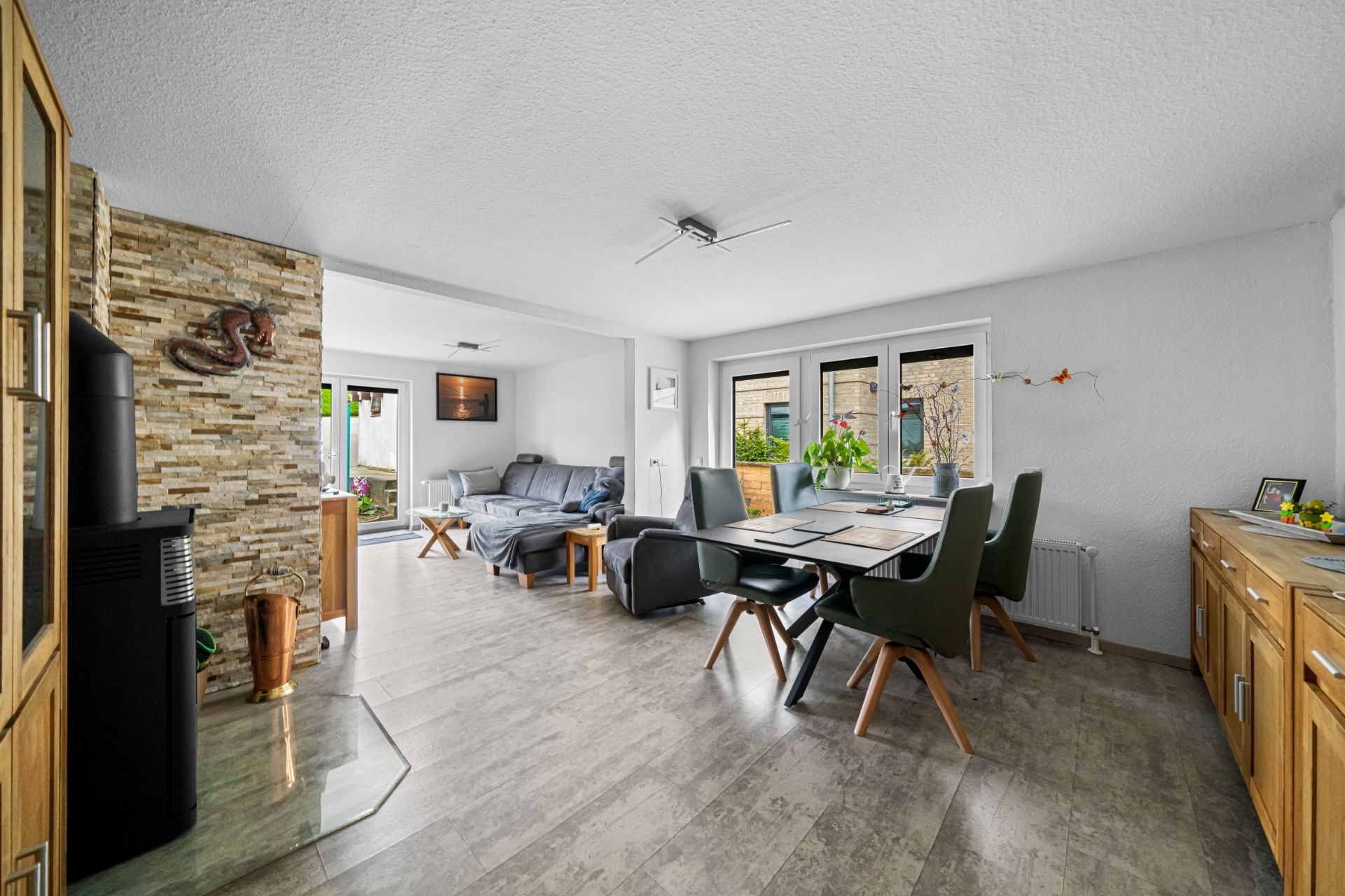 Helles Wohn- und Esszimmer mit Esstisch, Stühlen, Sofa und großen Fenstern.