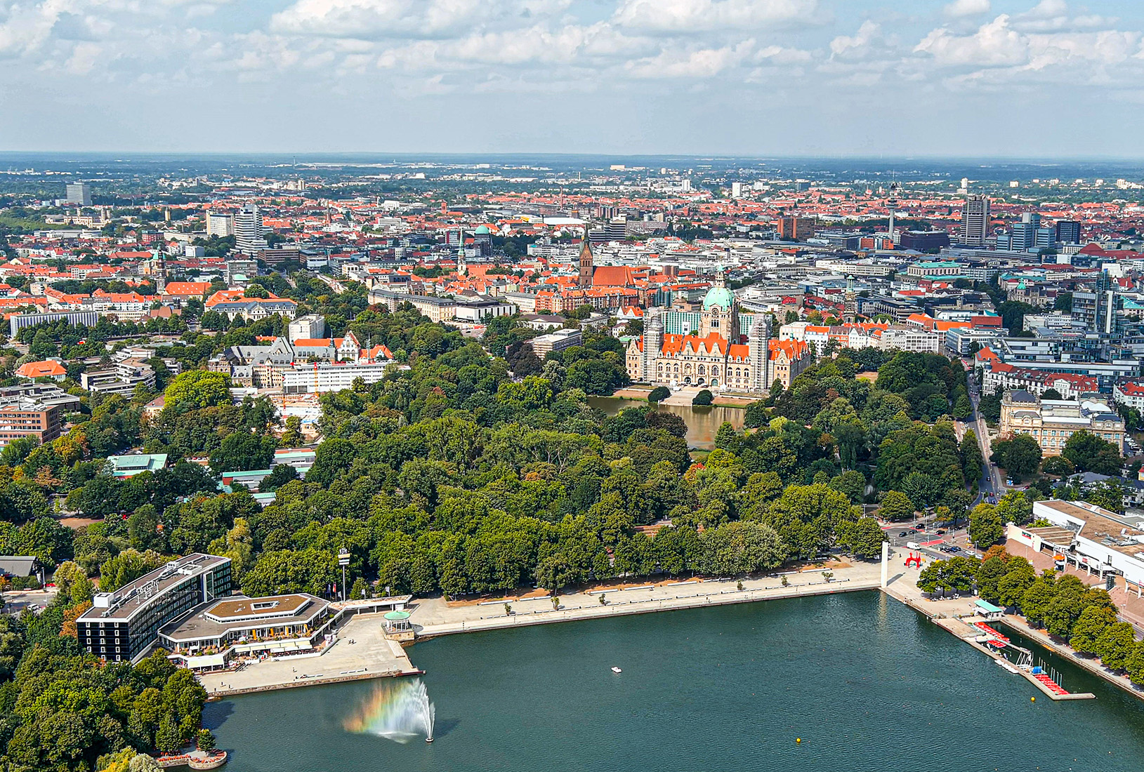 Luftaufnahme einer Stadt mit großem Park, Wasserfontäne im See und historischen Gebäuden.