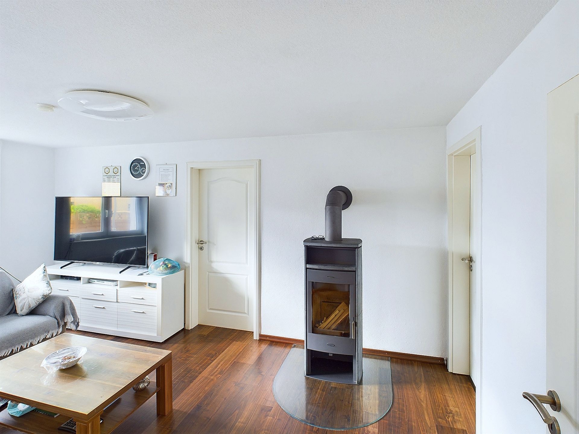 Wohnzimmer mit Holzofen, Fernseher, Couch und Holztisch auf Holzfußboden.